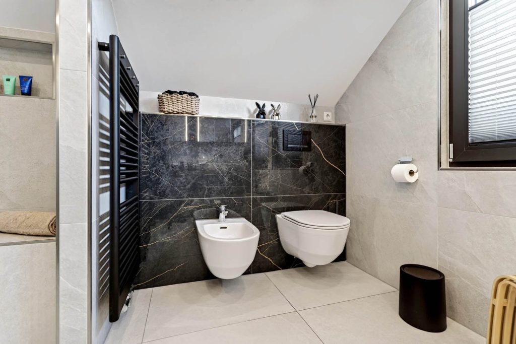 WC-Bereich mit Bidet und Wand-WC vor großformatigen Fliesen in dunkler Marmoroptik