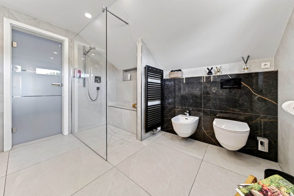 Gesamtansicht mit Glasdusche, schwarzem Heizkörper und WC-Bereich in dunkler Marmoroptik