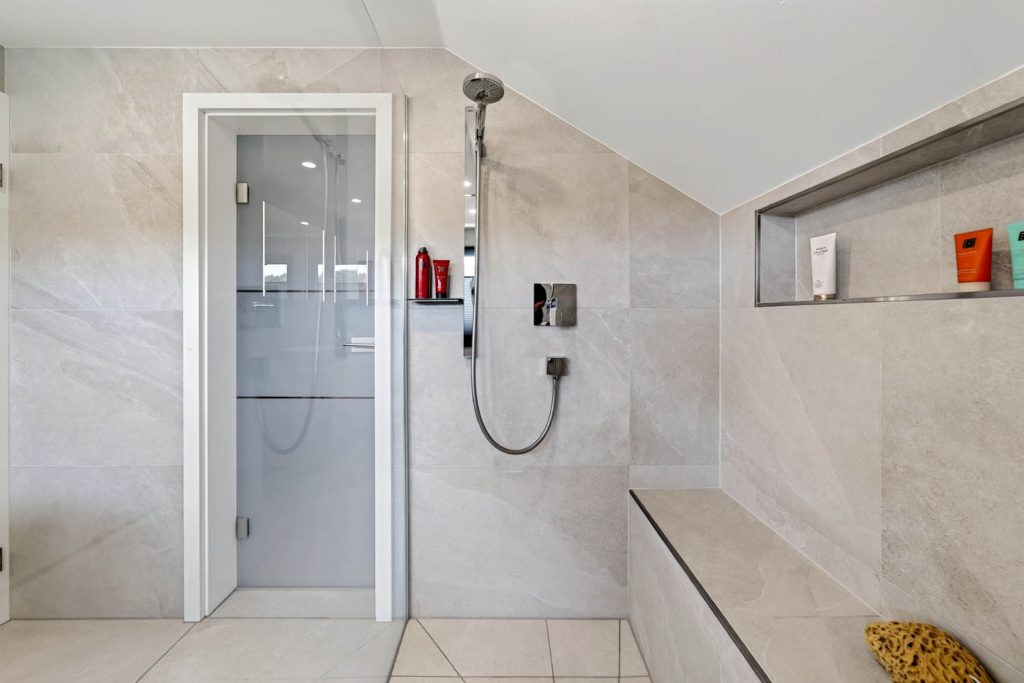 Begehbare Dusche mit Brausestange, Sitzbank und beleuchteter Wandnische unter der Dachschräge