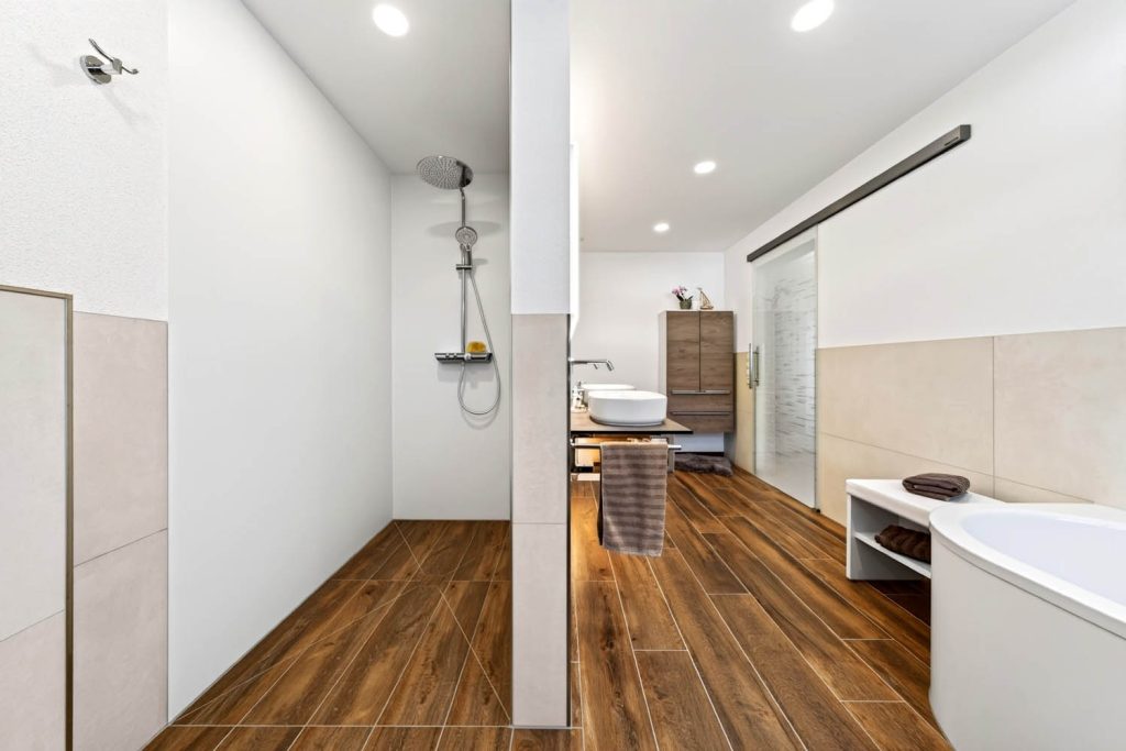 Blick in die bodengleiche Dusche hinter der Vorwand, rechts Wanne und Hochschrank