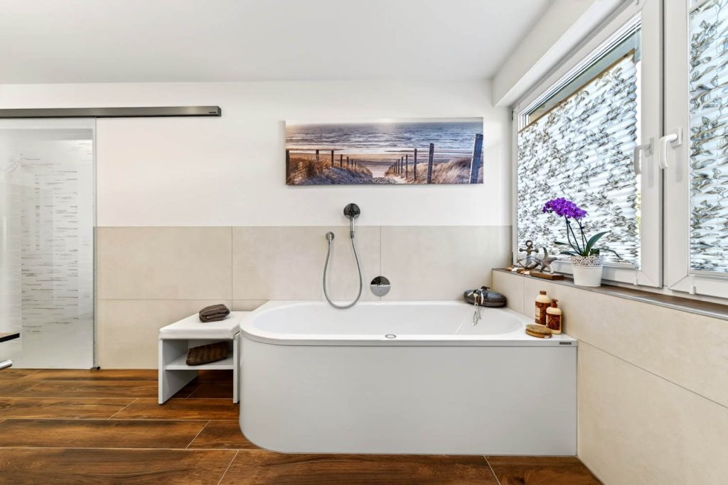 Badewanne mit Sitzbank unter einem Wandbild, rechts das Fenster mit Orchidee