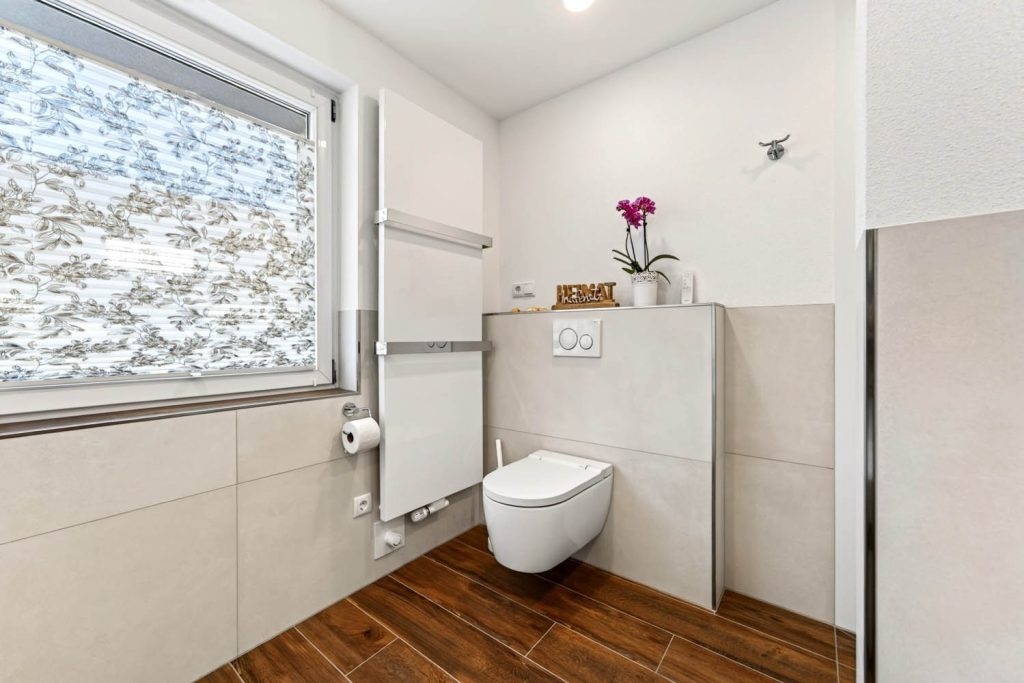 Wand-WC vor halbhoher Vorwand unter dem Fenster, daneben Handtuchheizkörper