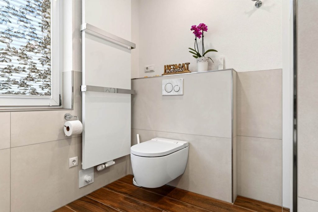 Wand-WC vor gefliester Vorwand mit Ablage und Orchidee, links Heizkörper