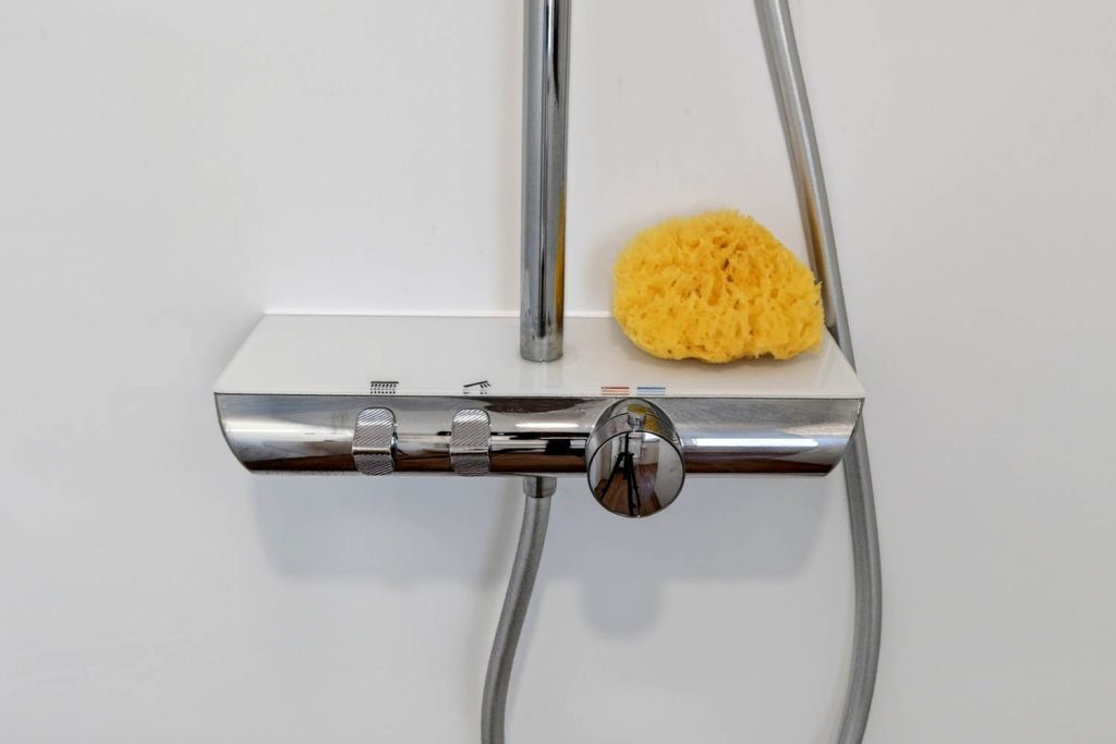 Thermostat mit Ablagefläche und Naturschwamm an der weißen Duschwand
