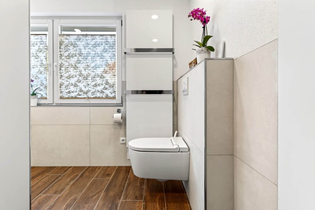 Wand-WC neben Hochschrank, im Hintergrund Fenster und Handtuchheizkörper