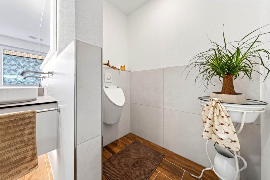 Urinal hinter einer Trennwand, links das Waschbecken mit Handtuch