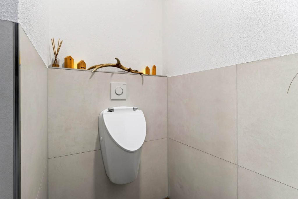 Urinal vor gefliester Vorwand, auf der Ablage Deko aus Holz