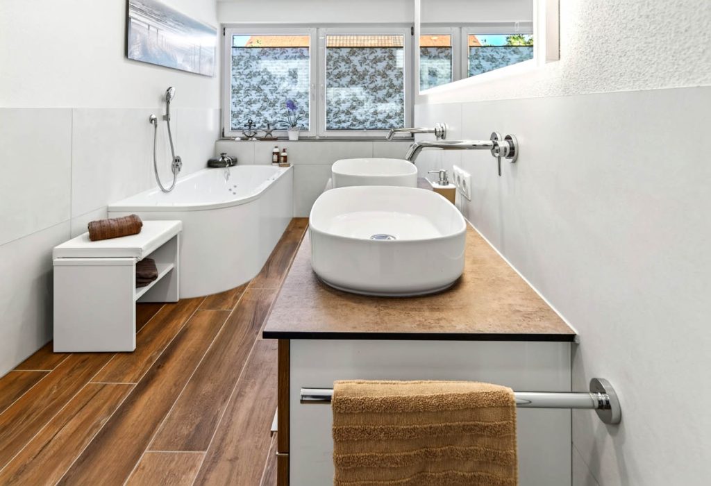 Waschtisch mit Aufsatzbecken im Vordergrund, dahinter Badewanne und Fenster