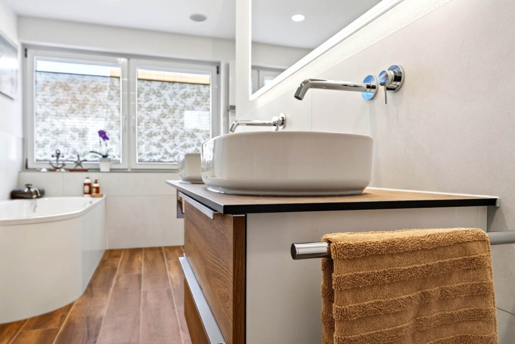 Aufsatzbecken mit Wandarmatur und Handtuch, im Hintergrund die Eckbadewanne