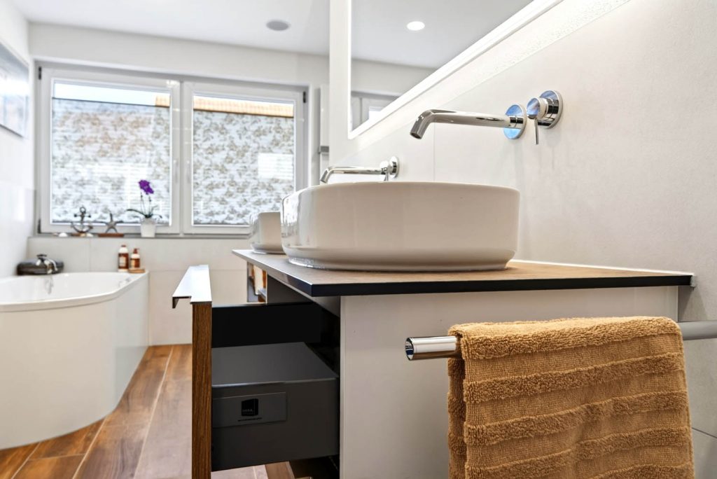 Waschtisch mit geöffneter Schublade, dahinter Badewanne und Fenster