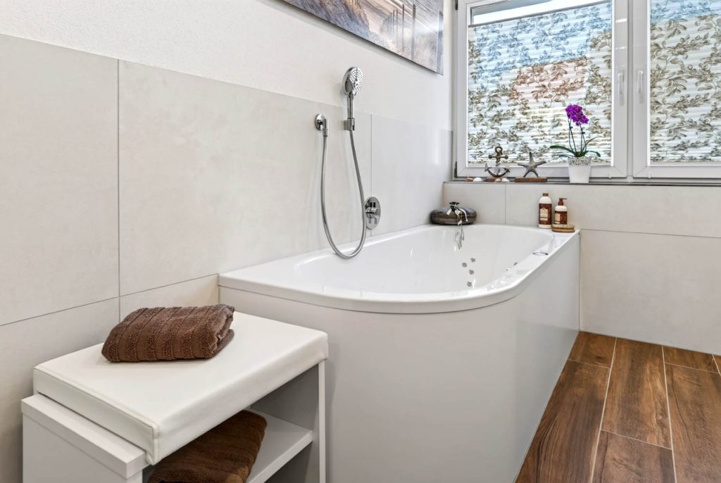 Badewanne mit Sitzbank und Handbrause an der gefliesten Wand