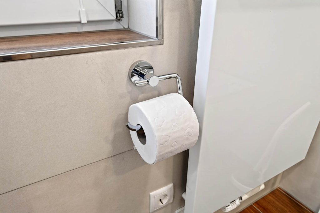 Toilettenpapierhalter in Chrom an der hellen Fliesenwand