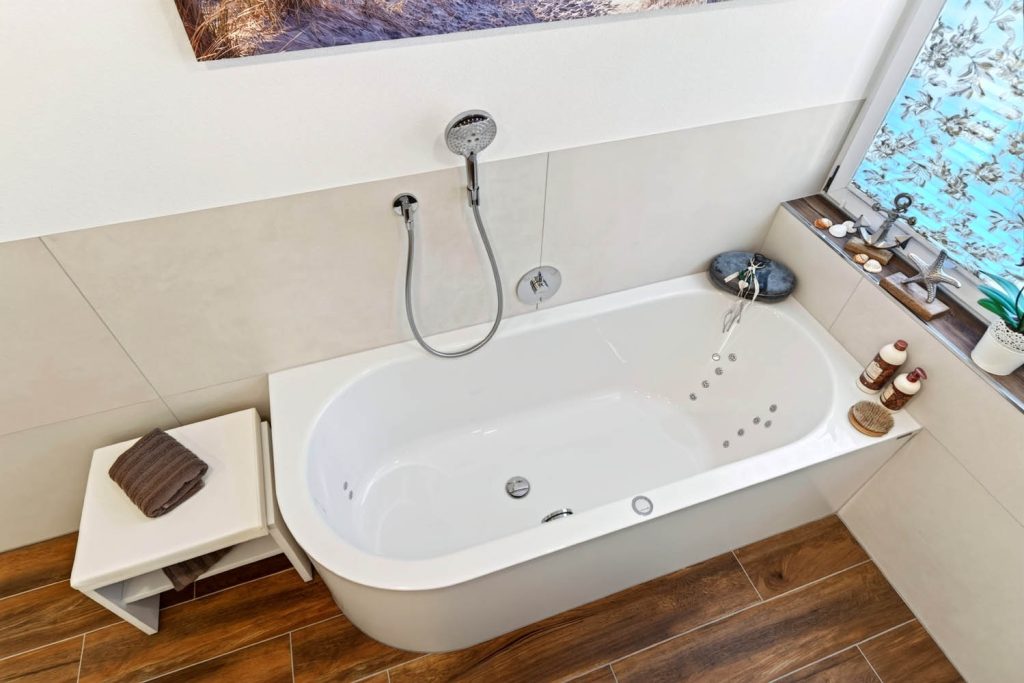 Badewanne mit abgerundeter Ecke und Sitzbank vor heller Fliesenwand