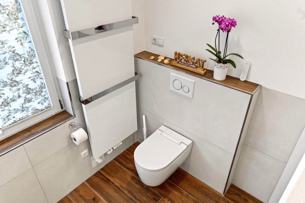 Wand-WC mit Vorwandablage, Orchidee und Handtuchheizkörper am Fenster