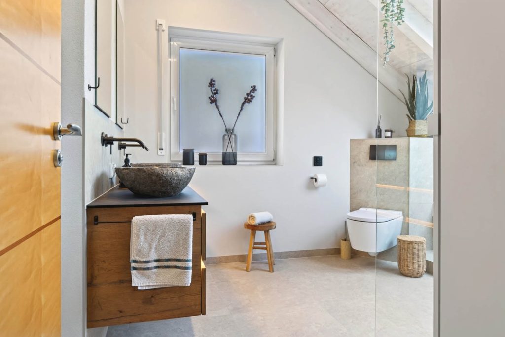 Blick durch die Tür: Waschtisch mit Natursteinbecken, Fenster und Wand-WC vor gefliester Vorwand