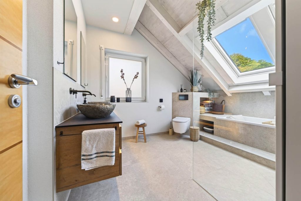 Dachgeschossbad mit Steinbecken auf Holzunterschrank, Wand-WC und Podestwanne unter dem Dachfenster