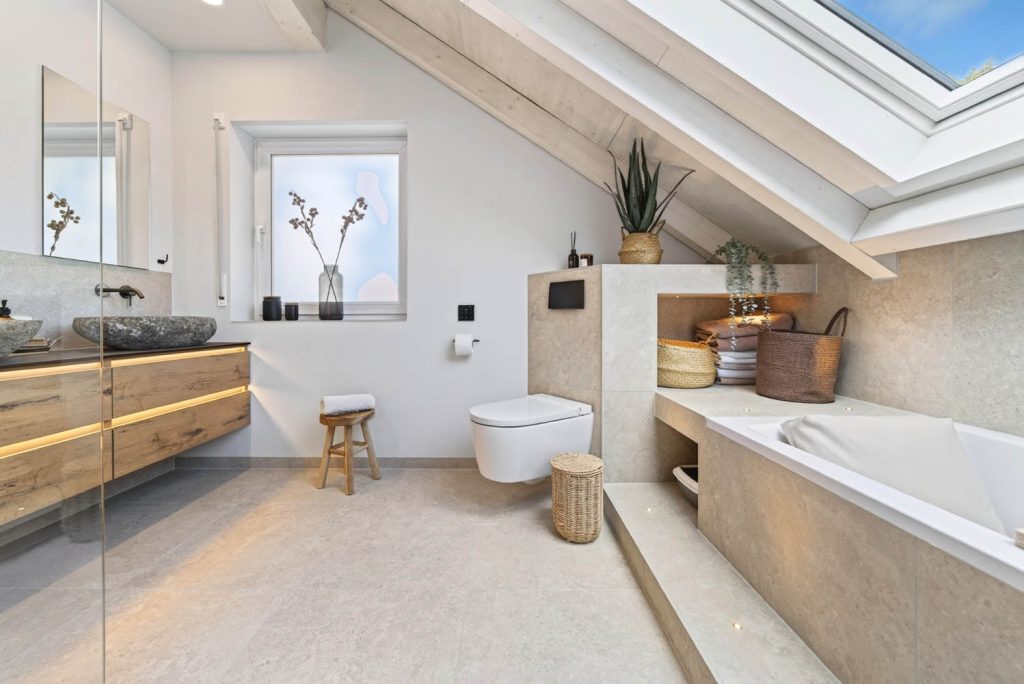 Raumansicht mit Waschtisch, Wand-WC und Podestwanne unter großem Dachfenster