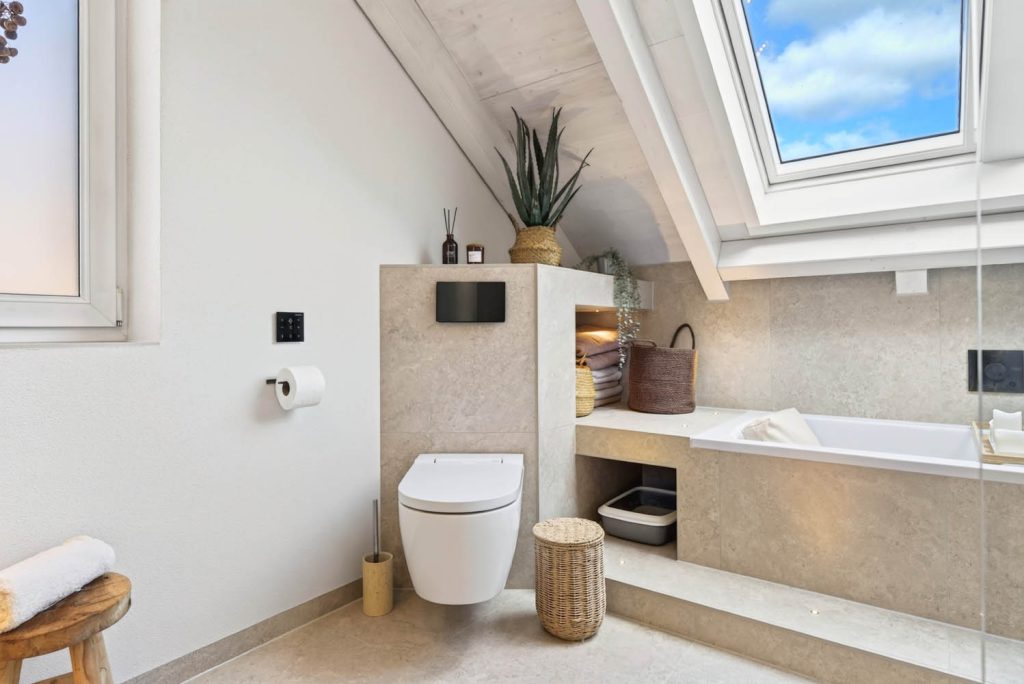 Wand-WC vor halbhoher Vorwand, dahinter die Badewanne mit Stufe unter dem Dachfenster