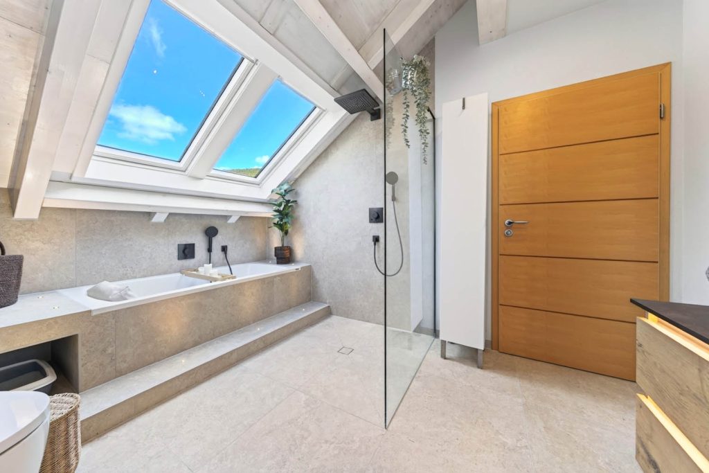 Dachfenster über der Badewanne, rechts Dusche hinter Glas und Holztür