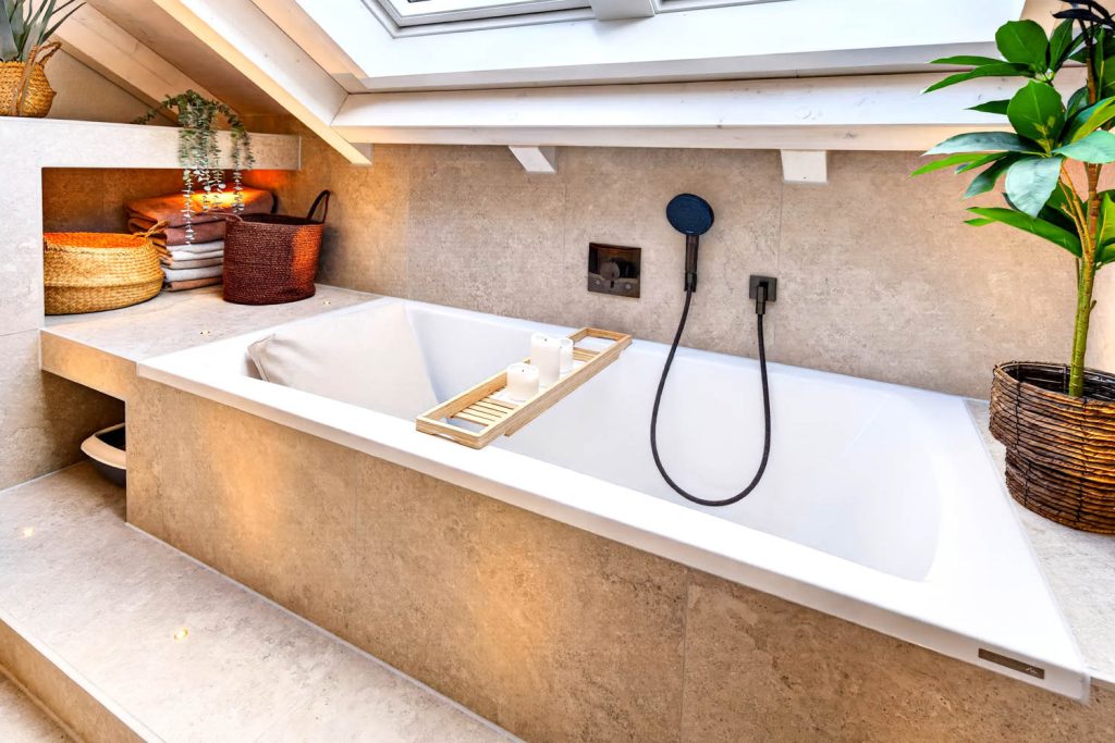 Badewanne mit Kopfkissen und Holzablage, daneben Pflanze im Korb