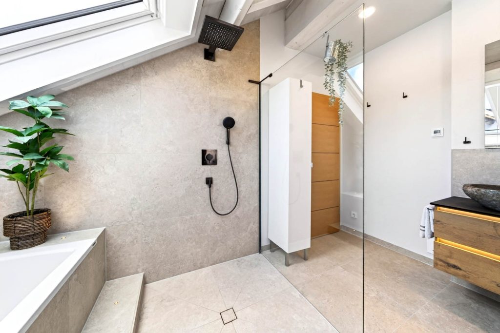 Bodengleiche Dusche mit schwarzer Kopfbrause, links die Badewanne