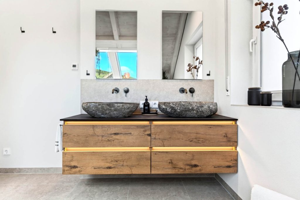 Doppelwaschtisch mit Natursteinbecken, schwarzen Wandarmaturen und zwei Spiegeln