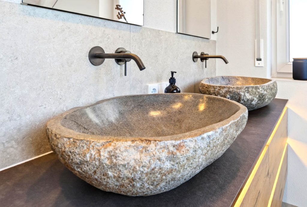 Zwei Waschbecken aus Flussstein mit Wandarmaturen in Schwarz