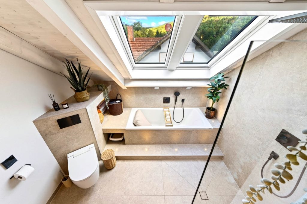 Blick von oben: Wand-WC, Podestwanne und Dusche unter dem großen Dachfenster