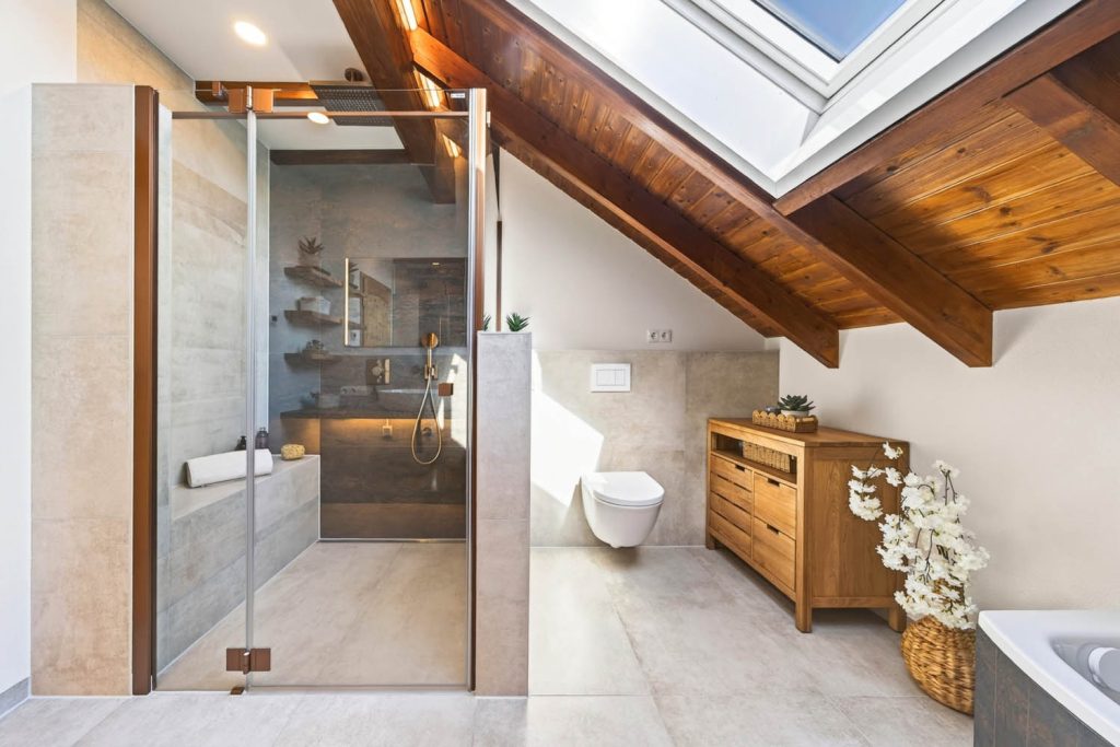 Dusche mit Glastür und dunkler Rückwand, rechts Wand-WC und Kommode aus Holz