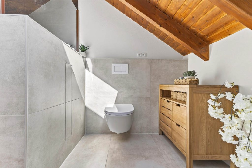 Wand-WC vor gefliester Vorwand, daneben Holzkommode und Blumendeko