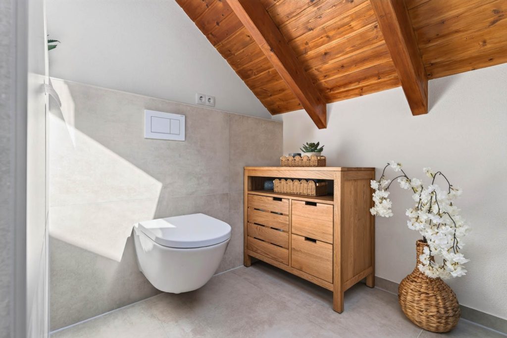 Wand-WC und Kommode aus Holz vor großformatigen Fliesen in Steinoptik