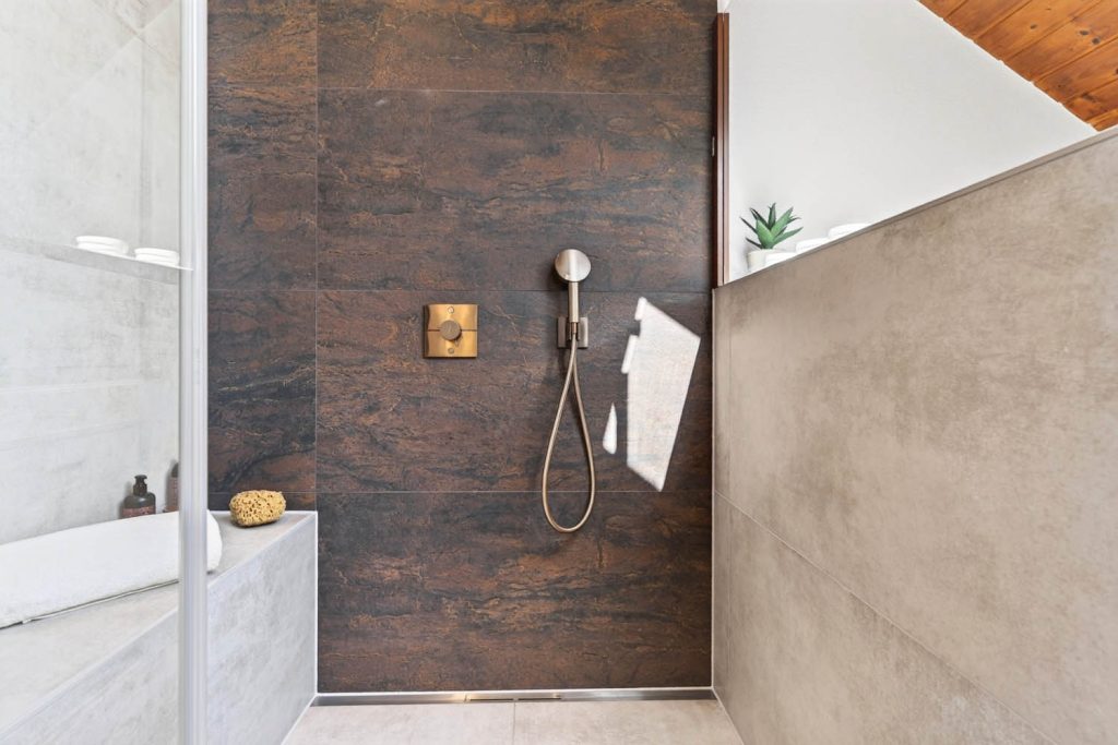 Dusche mit dunkler Rückwand in Rostoptik und Armatur in Kupfer