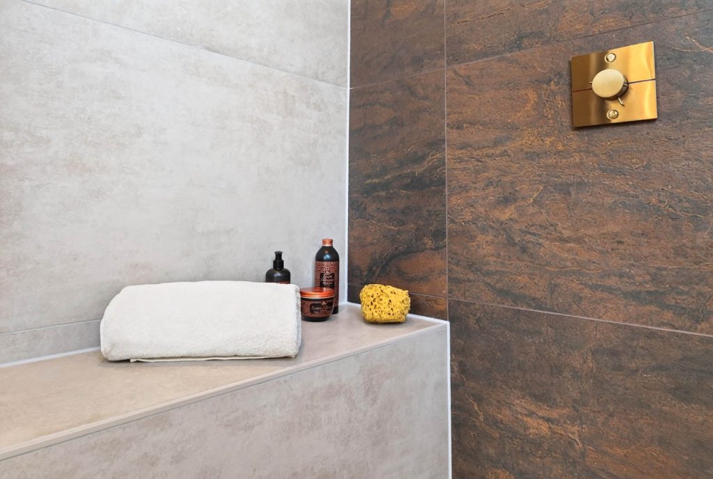 Geflieste Sitzbank in der Dusche mit Handtuch und Pflegeprodukten