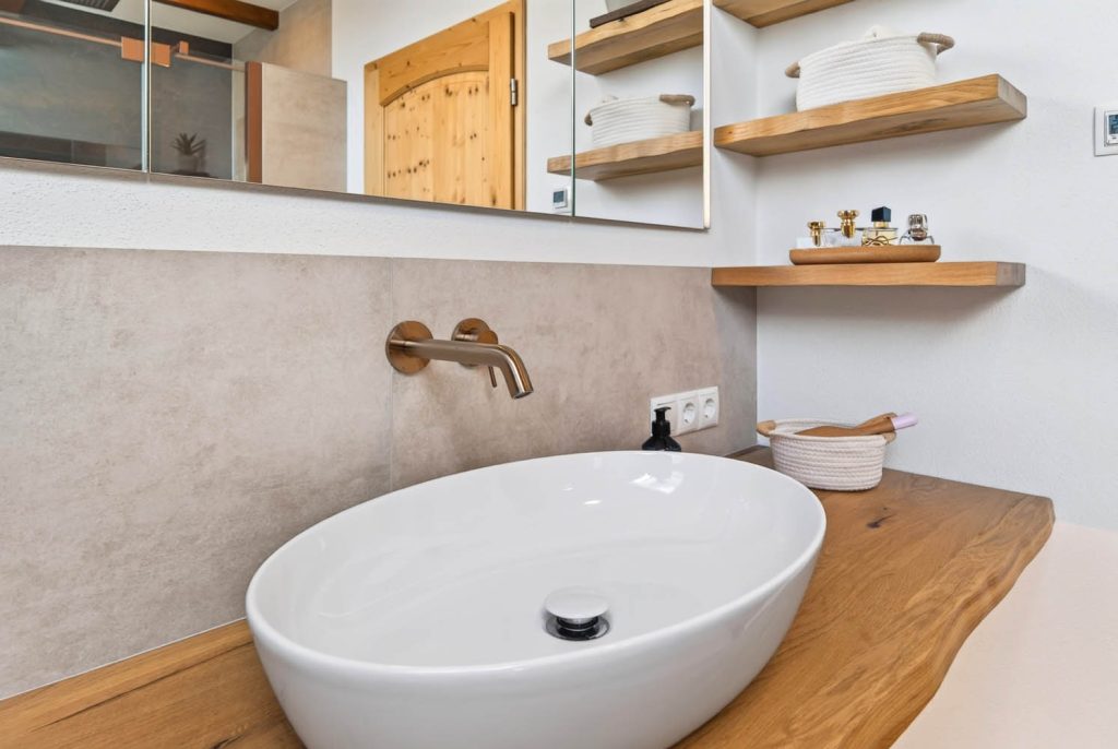 Ovales Waschbecken mit Wandarmatur, darüber Regale mit Deko
