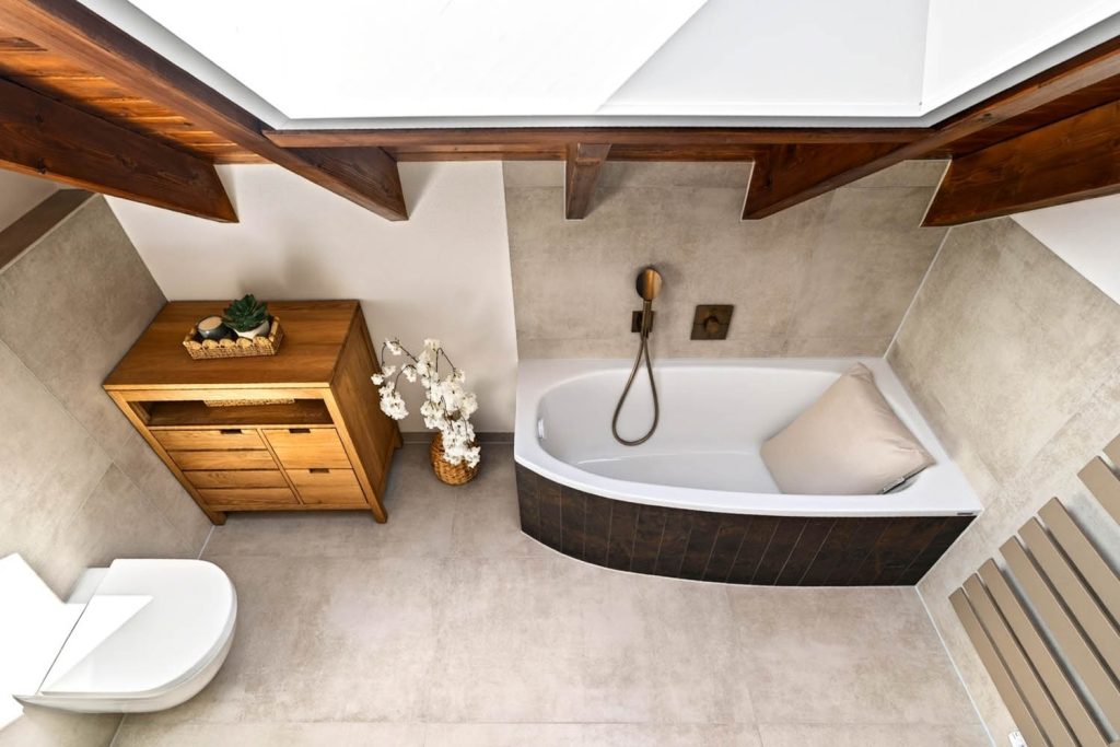 Eckbadewanne von oben mit Kommode aus Holz und Blumendeko