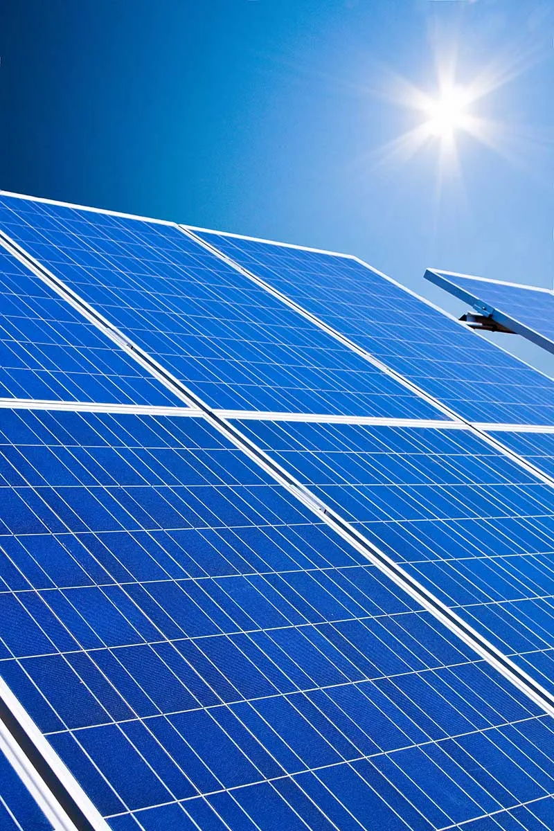 Blaue Photovoltaikmodule auf einer Aufständerung vor wolkenlos blauem Himmel mit strahlender Sonne