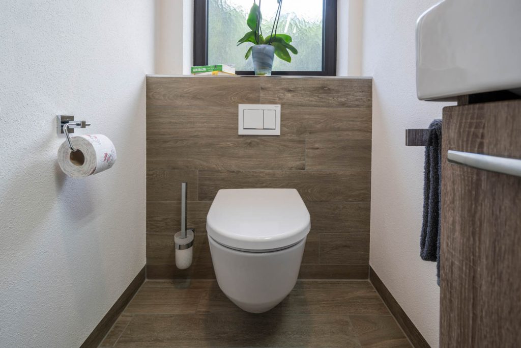 Wand-WC vor Vorwand in Holzoptik mit Ablage und Orchidee am Fenster