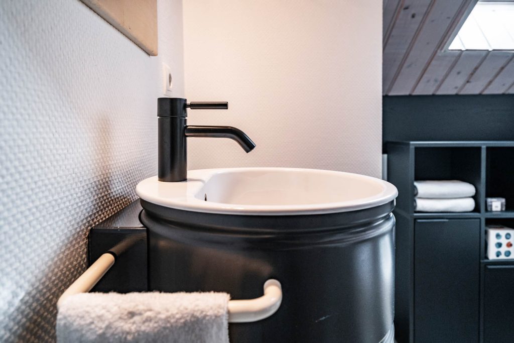 Waschbecken mit schwarzer Armatur, im Hintergrund Regal und Dachfenster