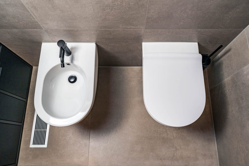 Bidet und Wand-WC auf grauen Fliesen von oben