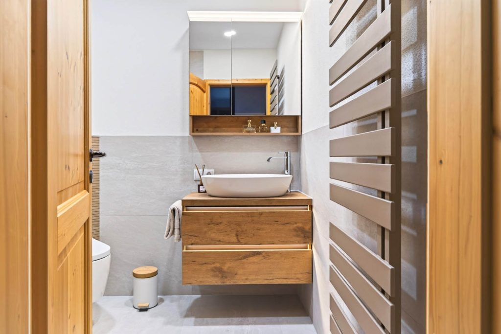 Waschtisch mit Holzfront und Aufsatzbecken, rechts ein Designheizkörper