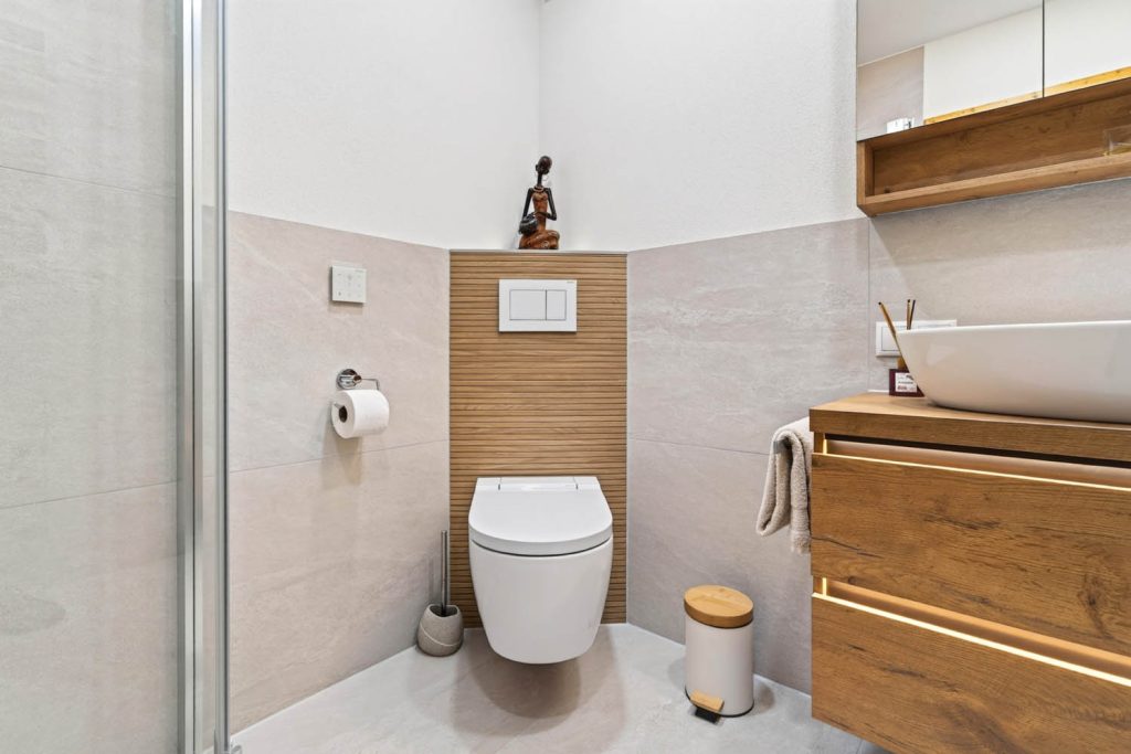 Wand-WC vor Lamellenwand in Holz, rechts der Waschtisch mit Lichtleiste