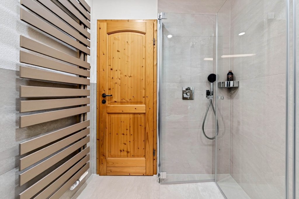 Glasdusche neben der Holztür, links der Designheizkörper