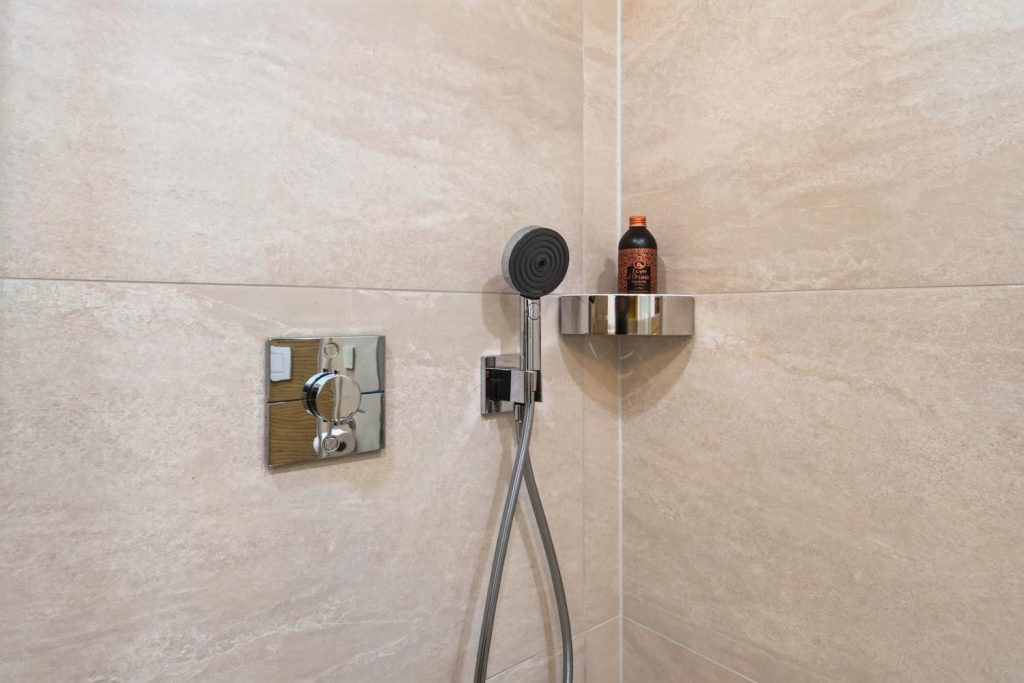 Thermostat, Handbrause und Ablage an der gefliesten Duschwand